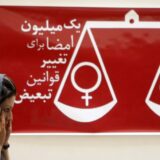 An Iranian woman walks past a banner reading "one million signatures to change the biased laws" and bearing a scale balancing female and male symbols during a press conference in Tehran, 27 August 2007. Iranians petitioning to achieve equal rights for women and men in Iran said today they hoped that their efforts would help change people's mentalities on the matter. AFP PHOTO/BEHROUZ MEHRI (Photo by Behrouz MEHRI / AFP)