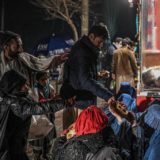 افغانستان - فقر و گرسنگی - A man distributes food to burqa clad Afghan women sitting in front of a bakery in Kabul on January 6, 2022. (Photo by Mohd RASFAN / AFP)