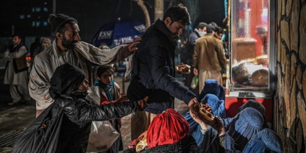 افغانستان - فقر و گرسنگی - A man distributes food to burqa clad Afghan women sitting in front of a bakery in Kabul on January 6, 2022. (Photo by Mohd RASFAN / AFP)