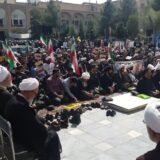 گروهی از آخوندها روی زمین با پلاکاردهای اعتراضی نشسته‌اند. مکان عکس مدرسه فیضیه قم است