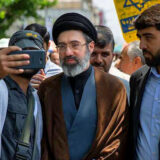 مجتبی خامنه‌ای، فرزند علی خامنه‌ای در میان دو نفر قرار دارد که یکی از آن‌ها با او در حال سلفی گرفتن است.