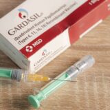 سوزن تزریق و جعبه واکسن "GARDASIL" روی پس زمینه قرار داده شده است.